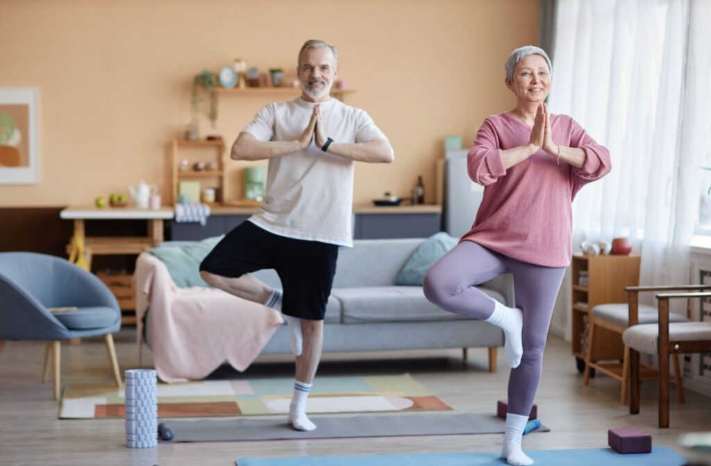 A pair of older adults performing leg raise exercises to improve their balance in their living room in senior living.
