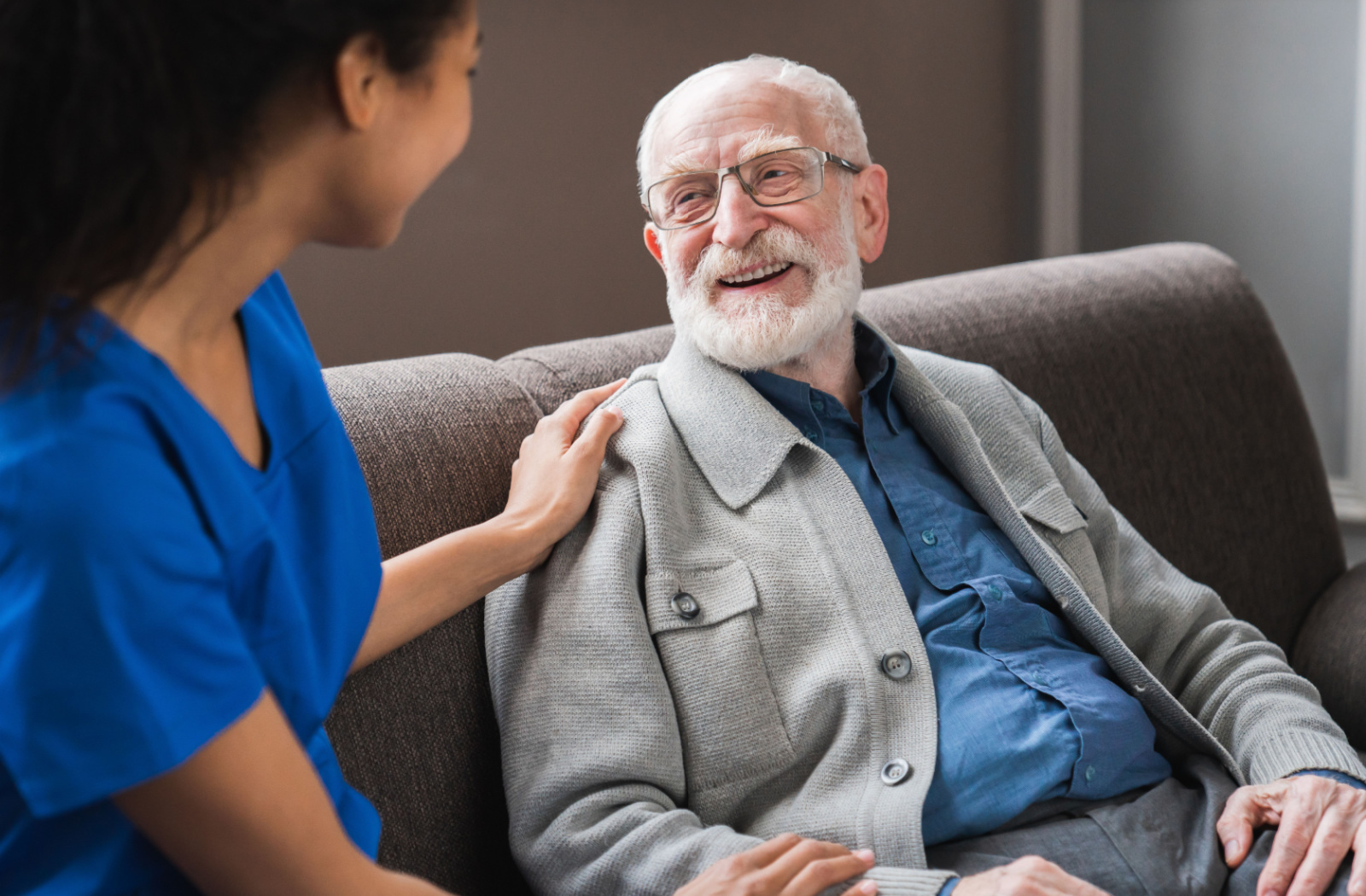 A caregiver comforts a smiling senior resident who is transitioning from assisted living to memory care.