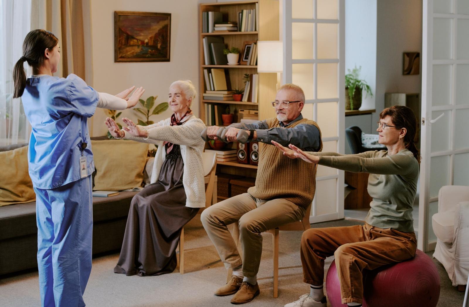 3 seniors participate in a light stretching activity under the guidance of a caregiver.