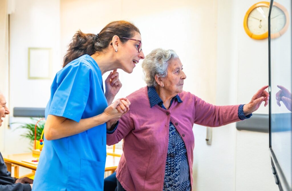 A caregiver assists an assisted living resident as they point to something written on a whiteboard.