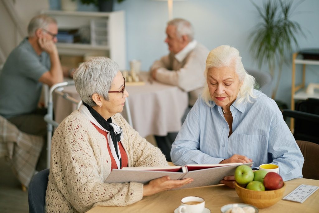 Two senior women are sharing memories by looking through a photo album in a retirement home